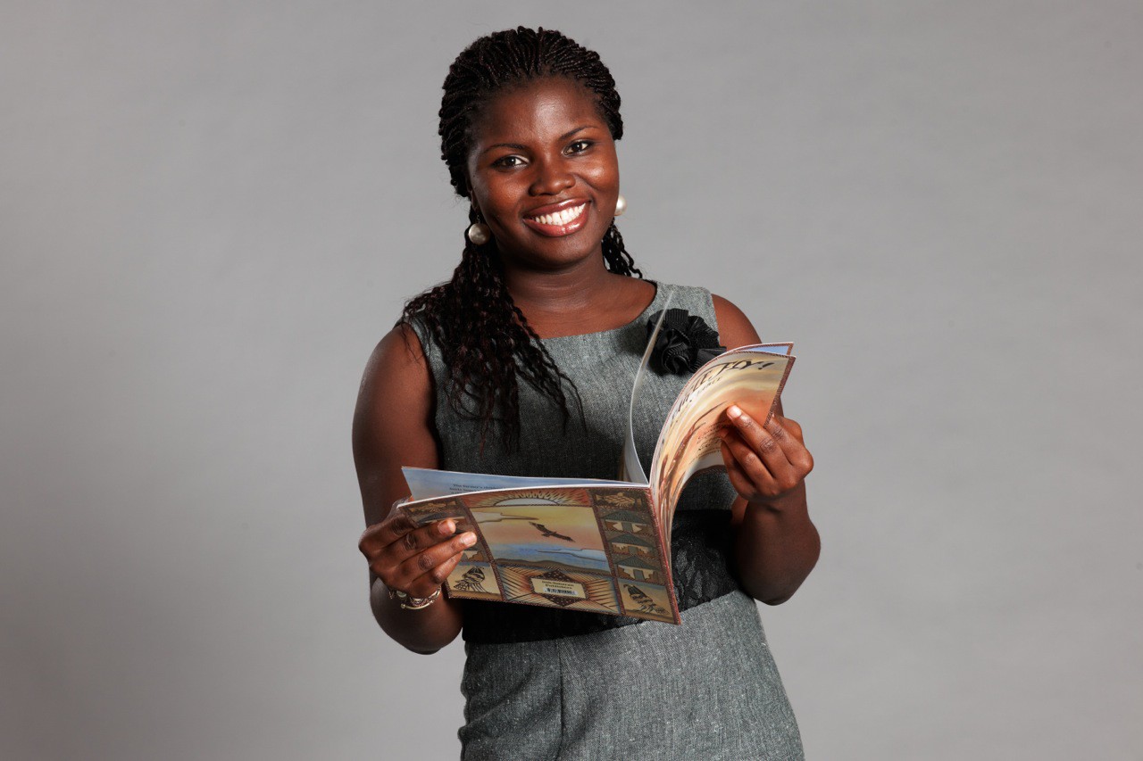 Deborah Ahenkorah smiles at the camera while holding a book open.